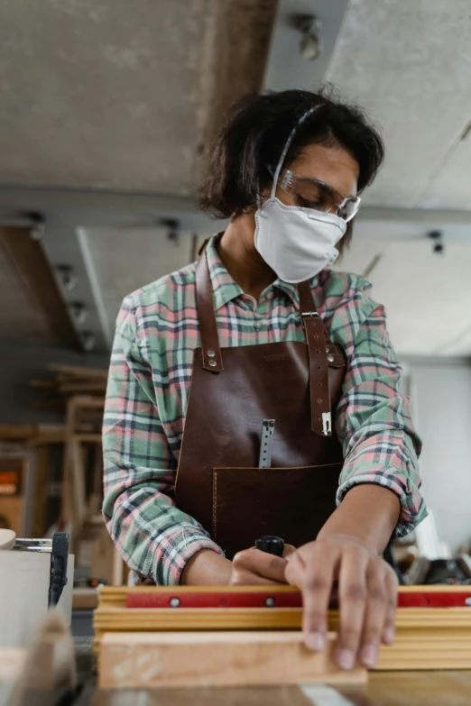 a woman working on a wood item with a face mask