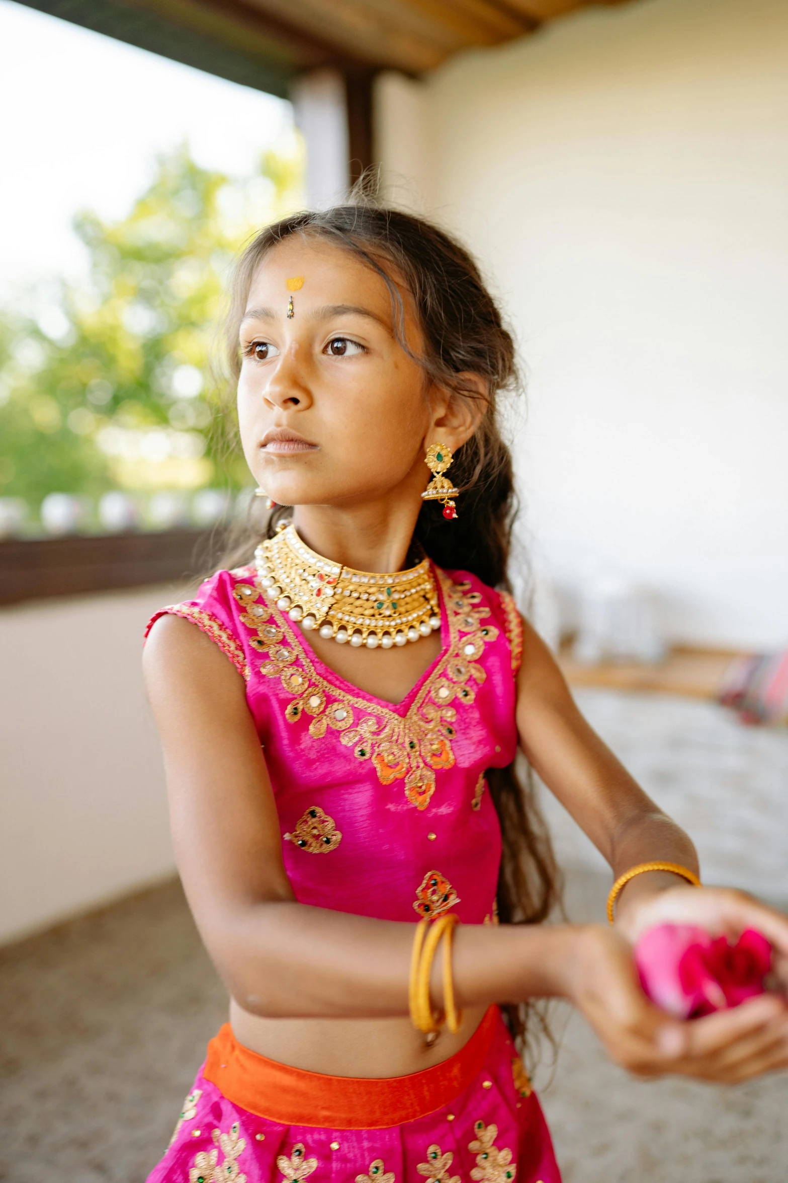 a small indian girl wearing a pink lehenga with an orange sash