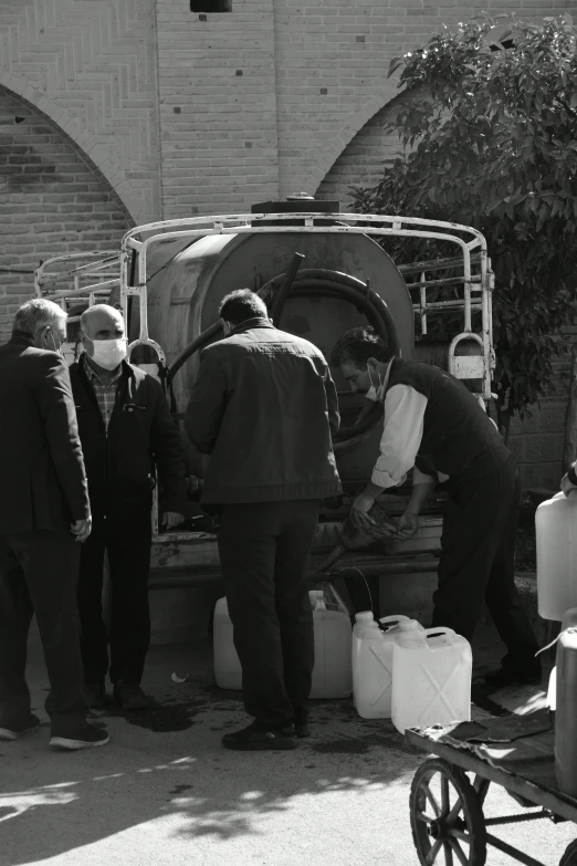 men and women in black suits and masks load large objects into the back of a truck