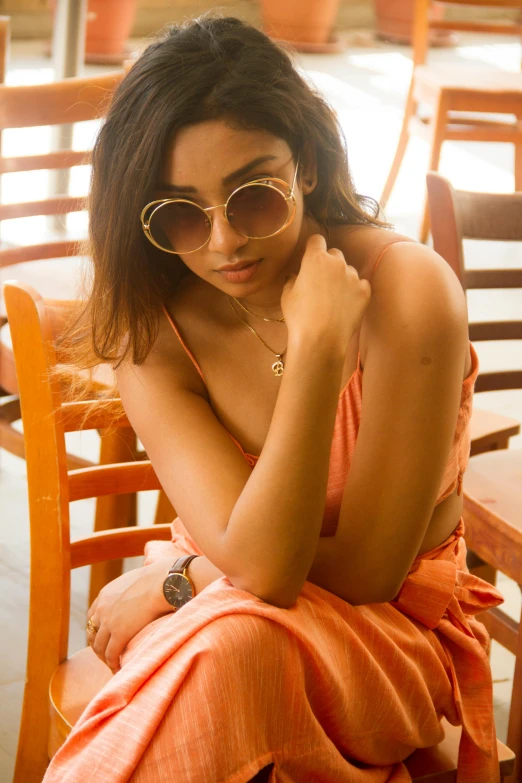 a beautiful young woman in a orange robe sitting next to a wooden chair