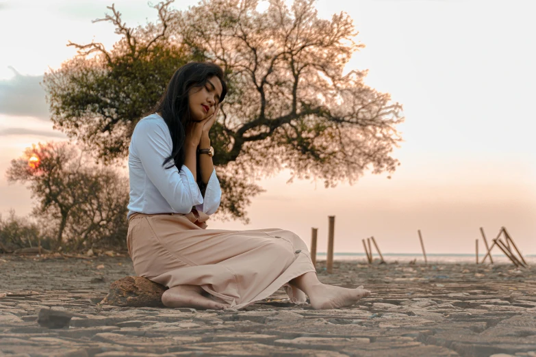 a woman sitting on the ground with her fingers to her face