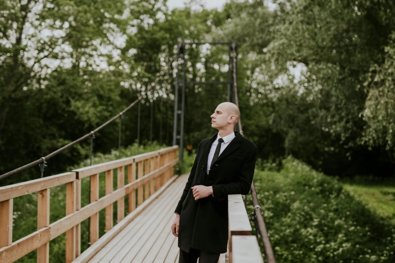 a man in suit and tie standing on wooden bridge