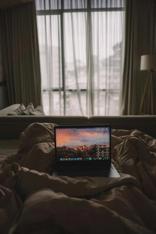 a small lap top sitting on a bed with a large window