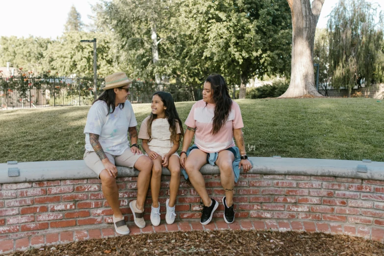 three girls sitting on a brick wall in the park