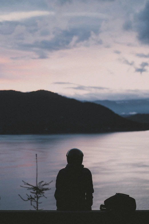 a person sitting near a body of water and a lake at dusk