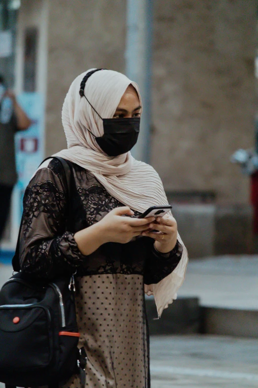 a woman in hijab and a mask checks her cell phone