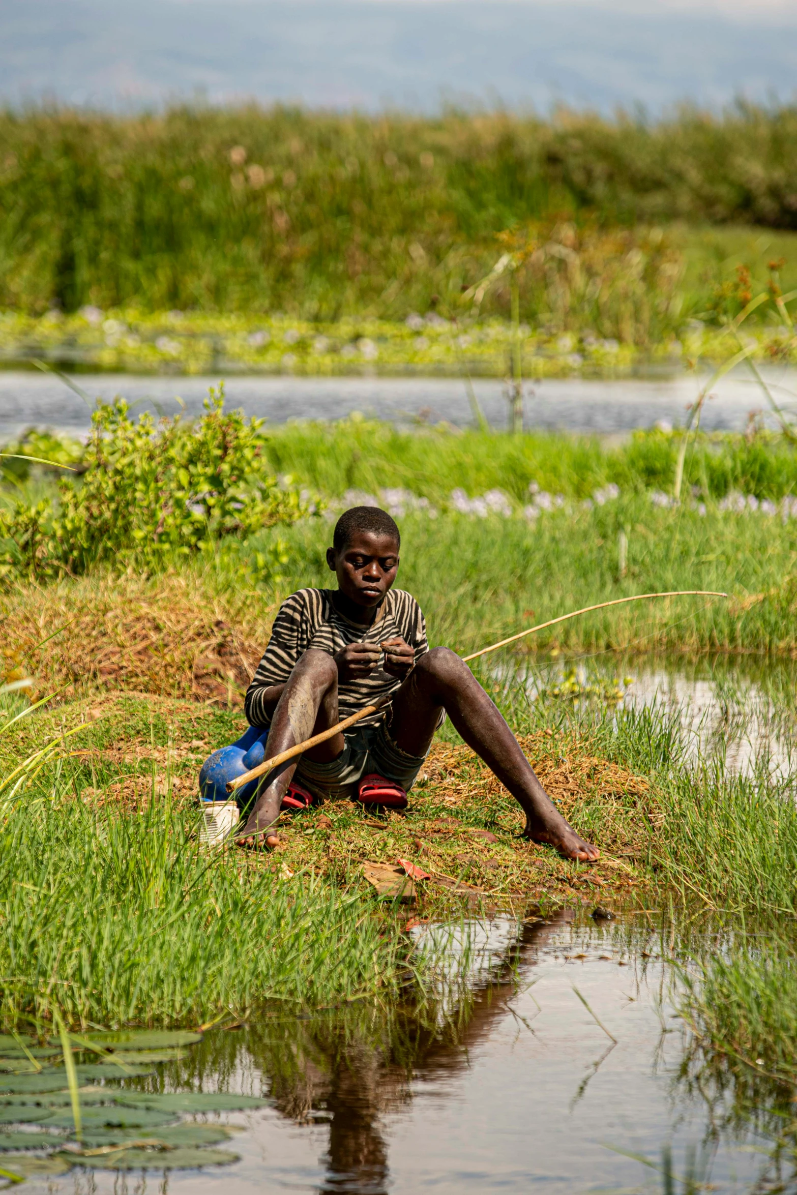 a man sits in the grass while he looks at the water