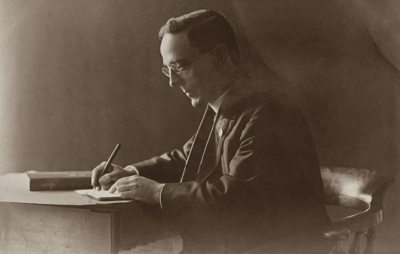 man seated at a desk writing with pen