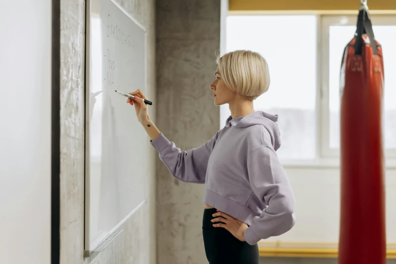 a woman writing on the whiteboard with a red kick - rope behind her