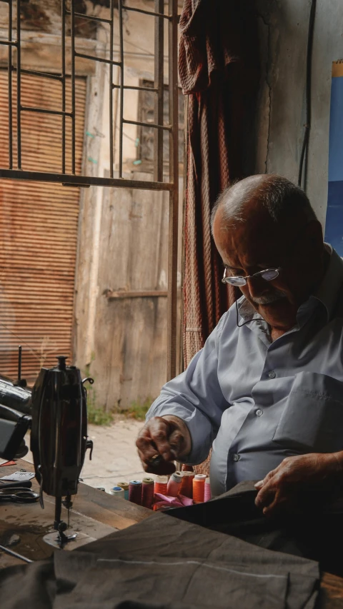 a man is sewing with his hands as he sits at the table