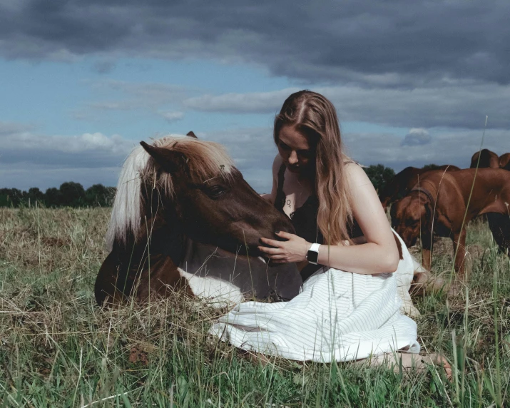 girl sitting in grass holding a cow while two other horses graze behind her