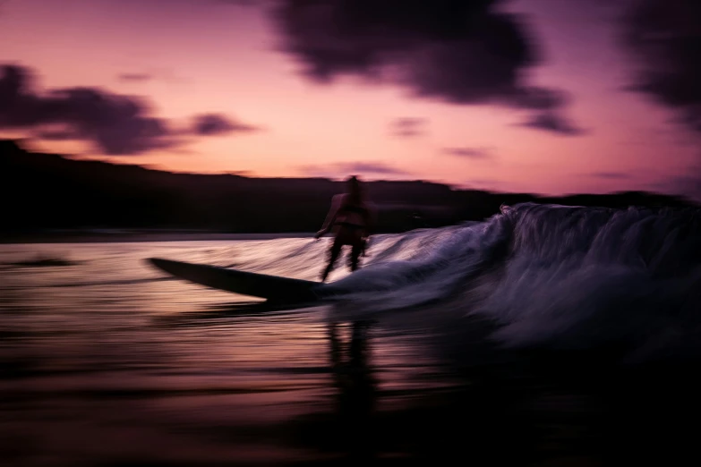 a surfer catches a wave as the sun sets