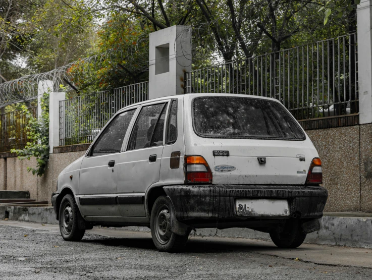 white hatchback car parked on street with fence in background