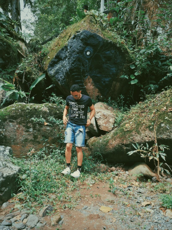 a man standing in the forest next to a big rock