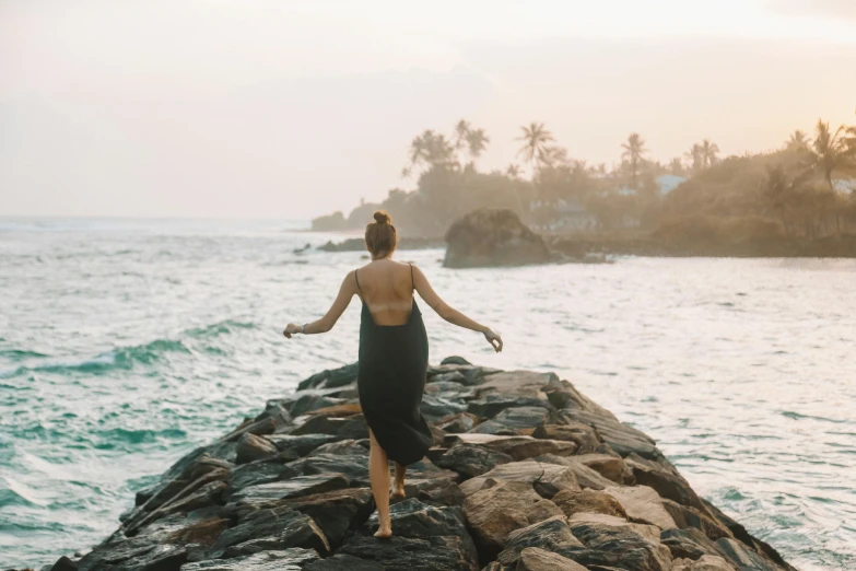 the woman is walking on the rocks by the water