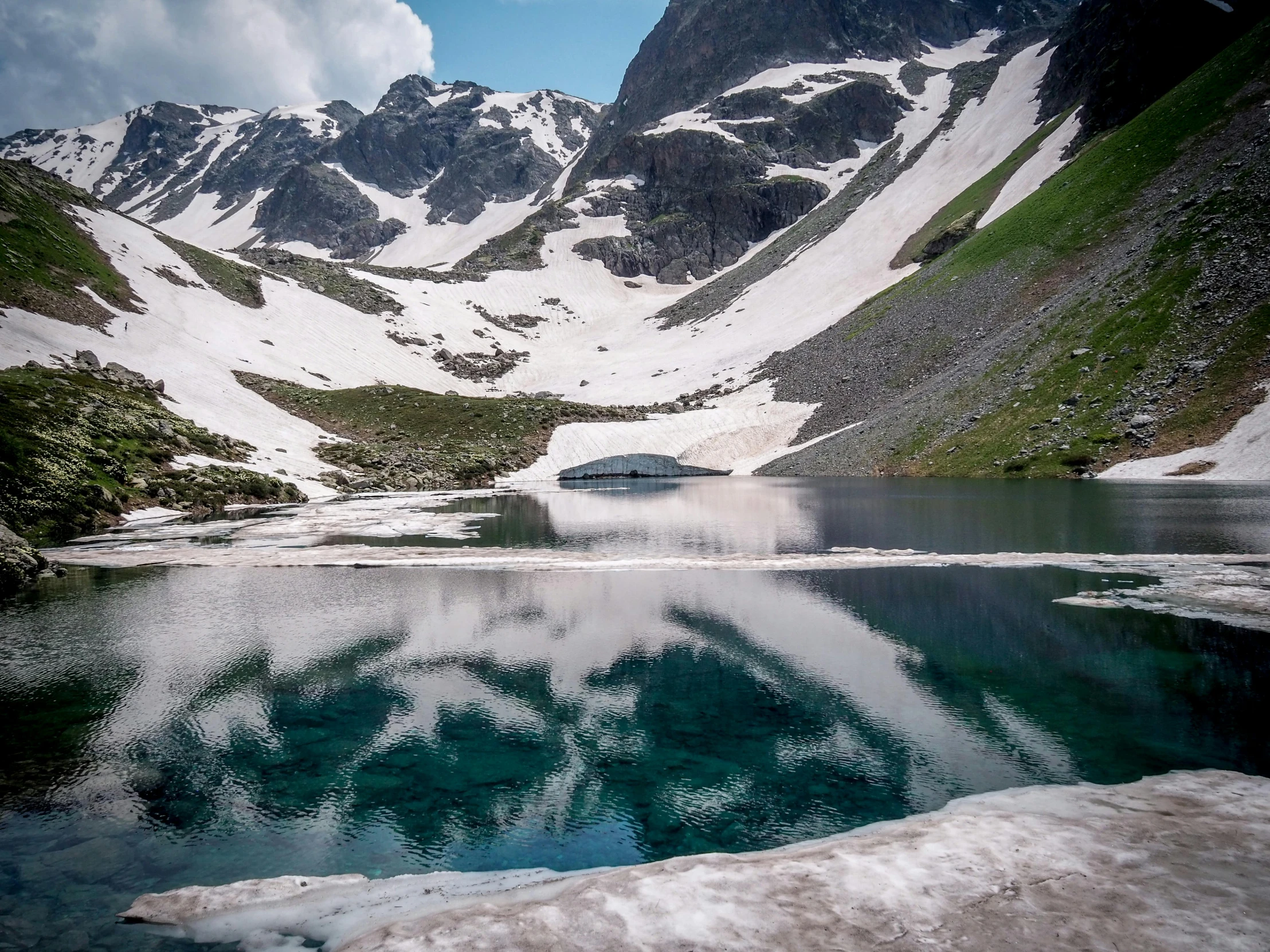 the snowy mountains are reflected in the small lake