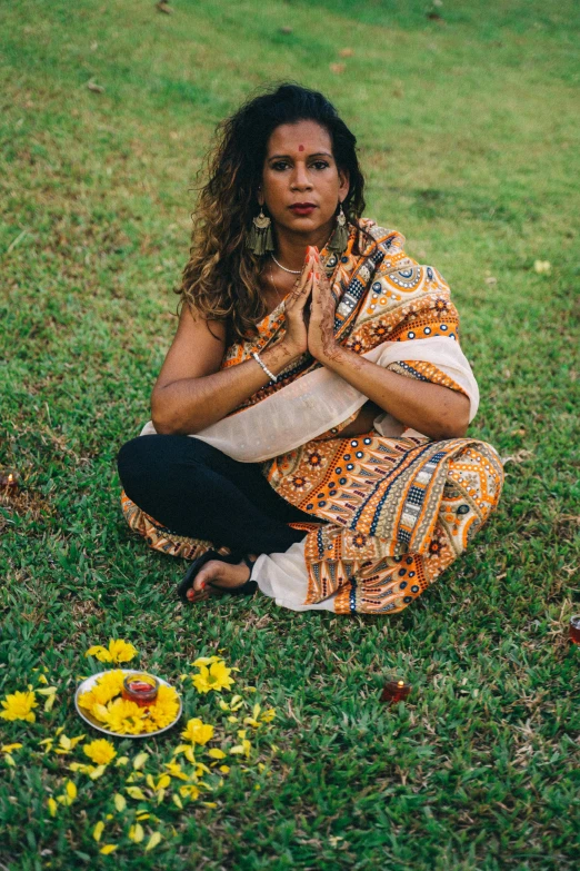 a woman meditating in the grass next to flowers