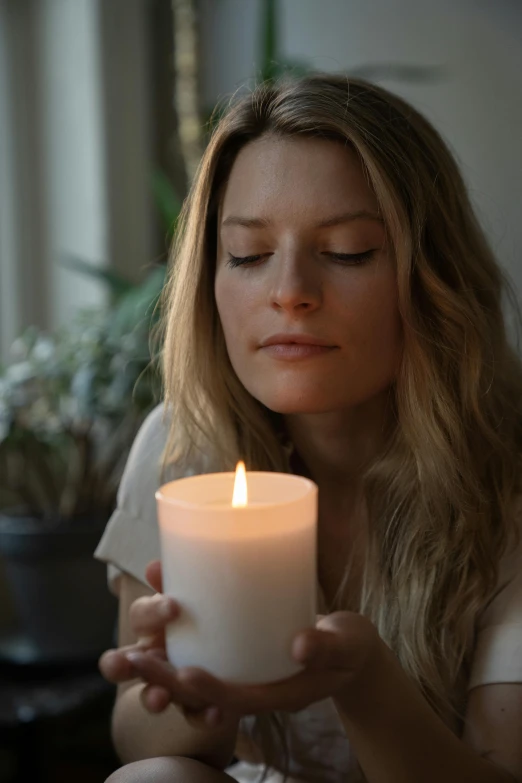 the woman is holding a white candle in her hands