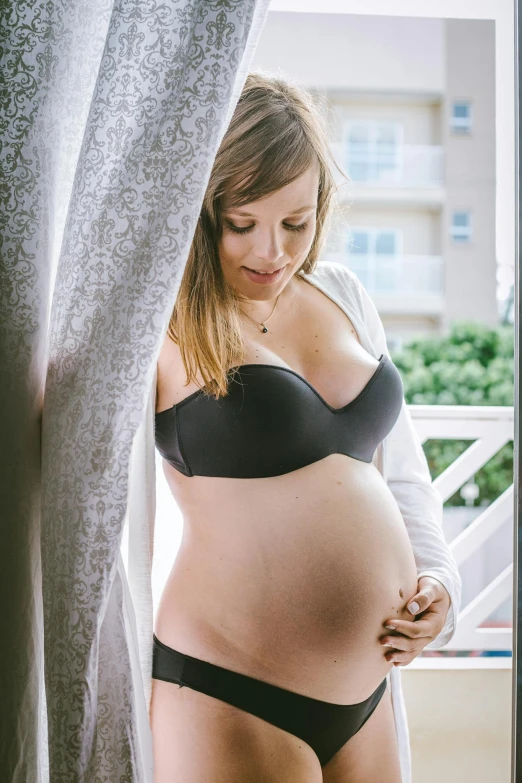 a pregnant woman in a black lingerie leaning on a window