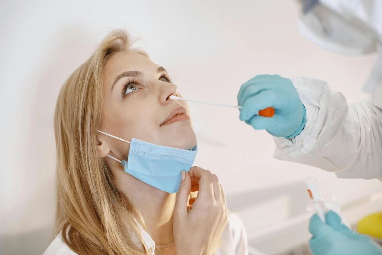 a woman with a mask and gloves on injecting into an iv