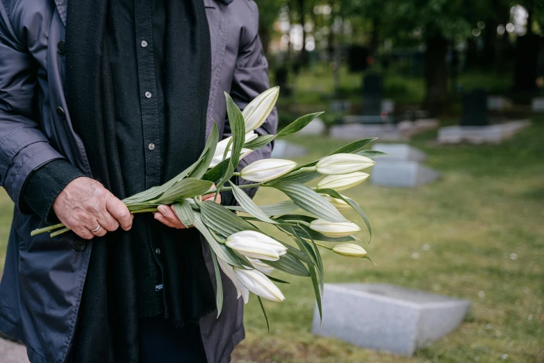 a man holding a bouquet of flowers while standing on a cemetery
