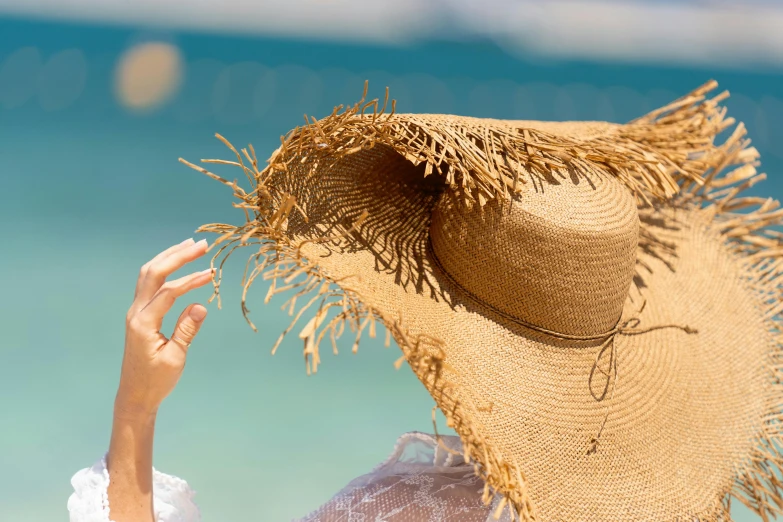 a person's hand under a straw hat by the water