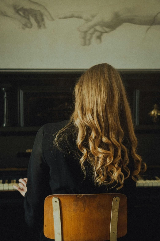 the back of a woman's head, sitting at a piano in front of an empty wall