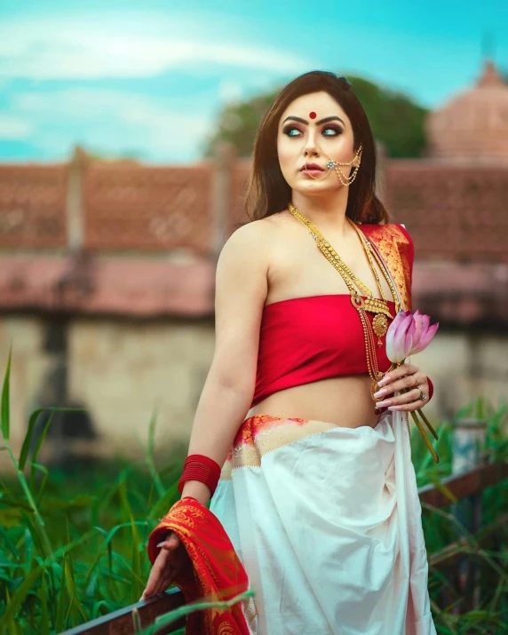 a woman in an indian outfit holding a pink flower