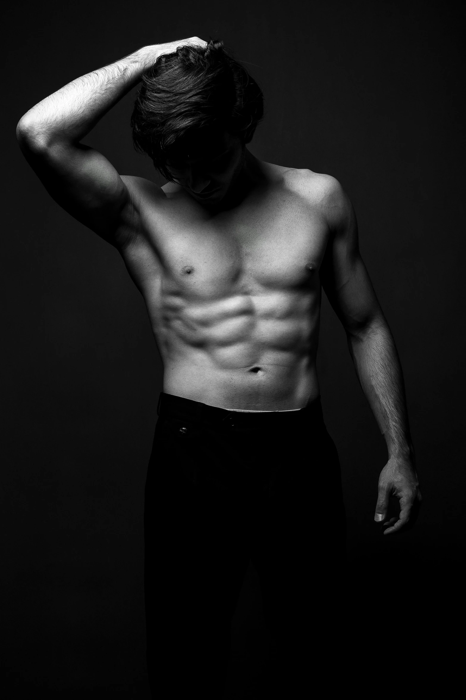 man without shirt standing against black backdrop and looking down