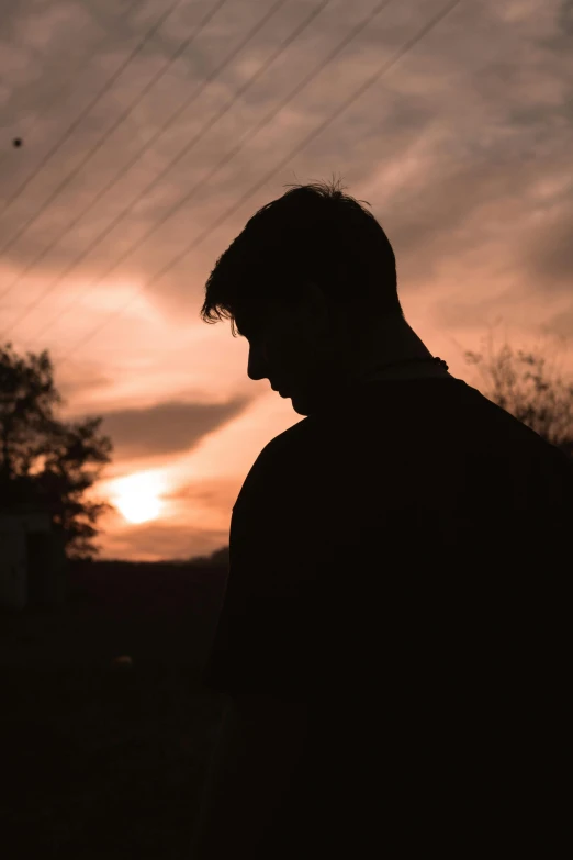 man at sunset staring down at his phone