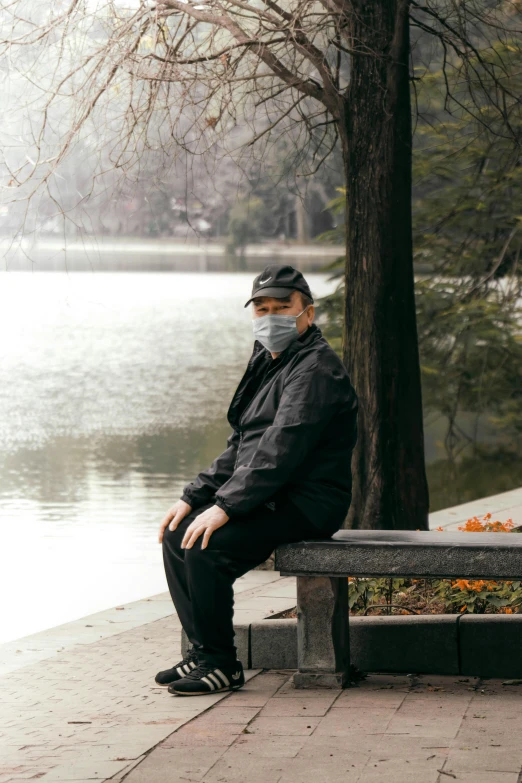 the man is sitting on the bench wearing a mask