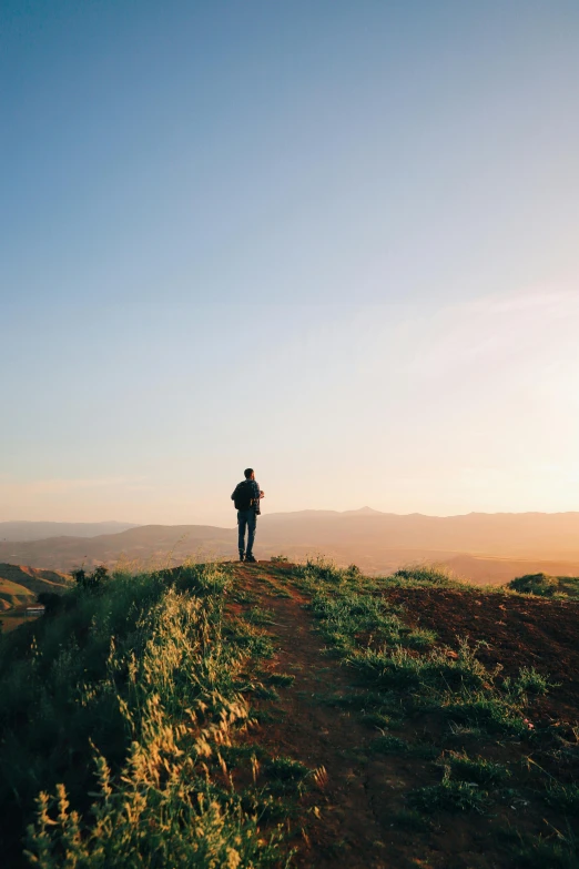 a lone person stands on a hill as the sun sets