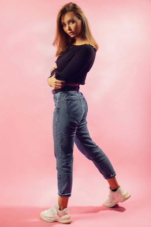 an attractive young woman in jeans posing on a pink background