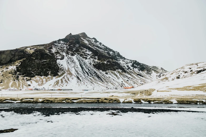 a snow covered mountain and water under a cloudy sky