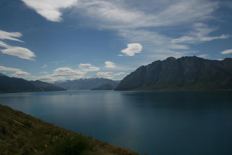 the mountain range on the side of a lake, with the sky above it