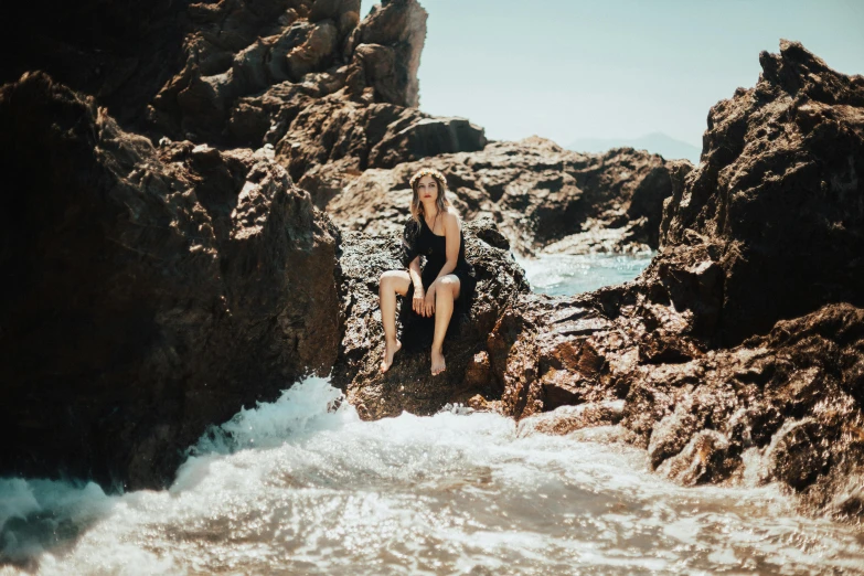 a girl in swimsuit sitting on rock next to the water