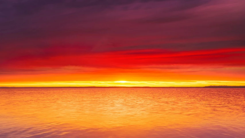 an ocean at sunset and red clouds with one boat