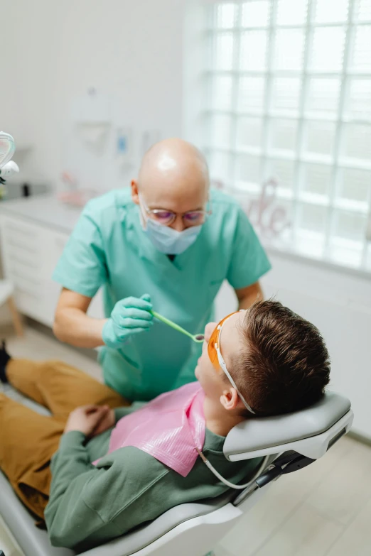 a child sitting in a chair with a dentist examining him