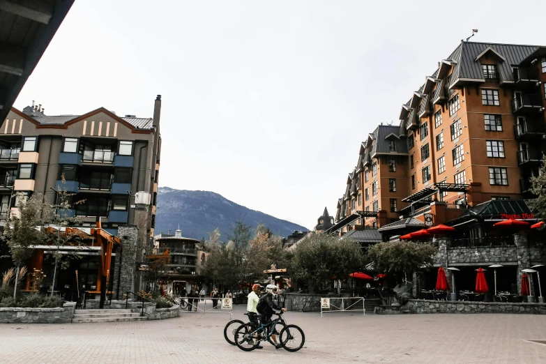 people are biking past several buildings and trees