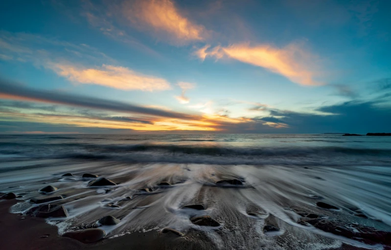 the sun setting on a wave hitting the sand