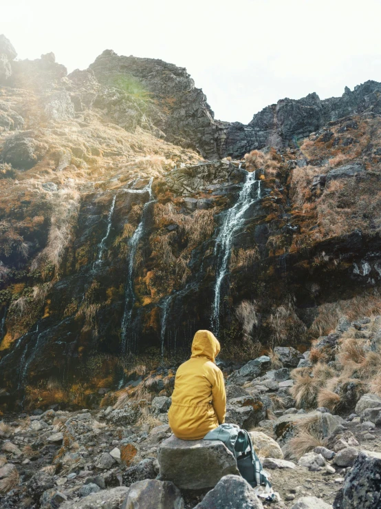 a person in a yellow jacket is sitting on a rock