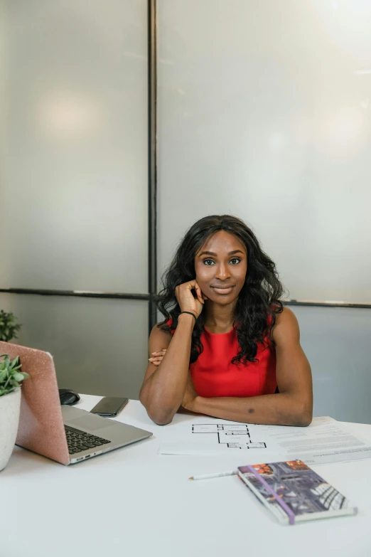 a lady in a red top and glasses sitting at a table with two laptops