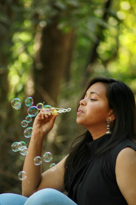 an asian woman sitting outside blowing bubbles on her finger
