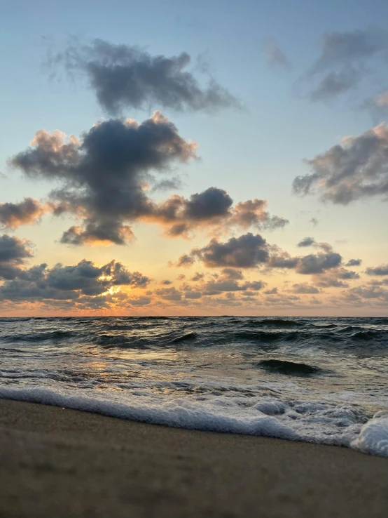 the sun setting behind clouds over the water on a beach