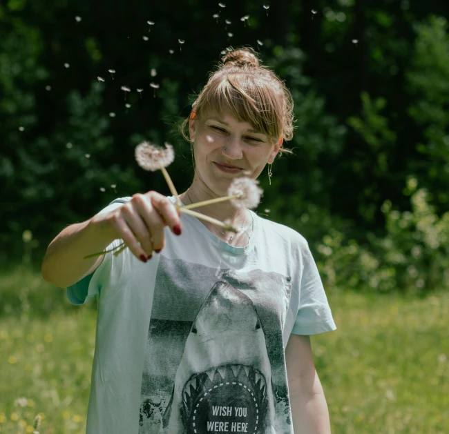 a young woman blowing on a dandelion outside