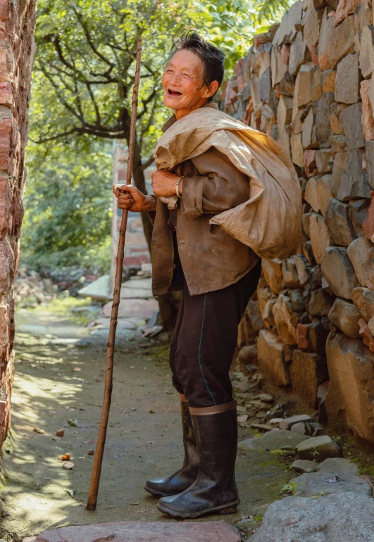 the man has on a jacket with a long hat and holding a stick