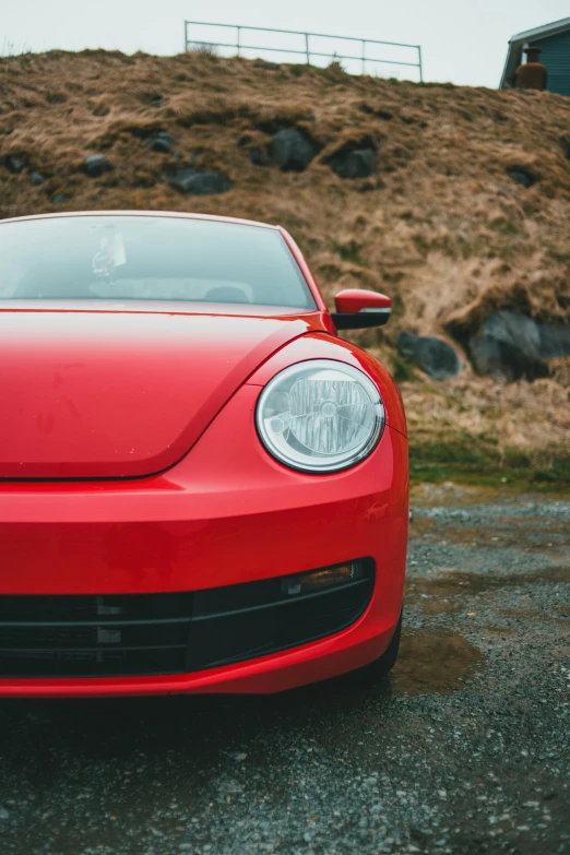 a close up of a red sports car parked in front of a hill