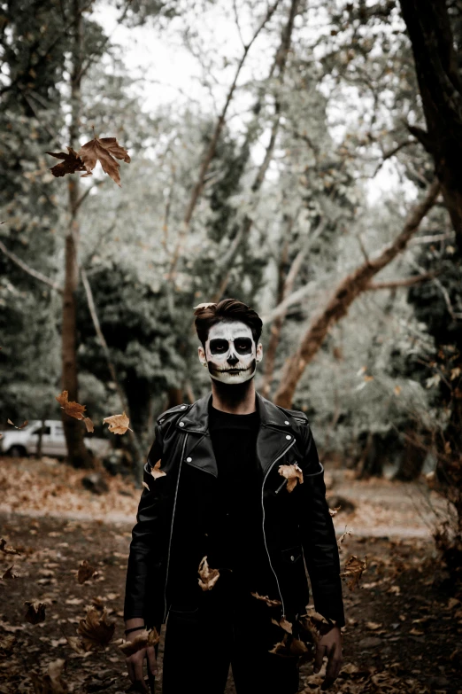 a man with a fake mask and skull face wearing a leather jacket in the woods