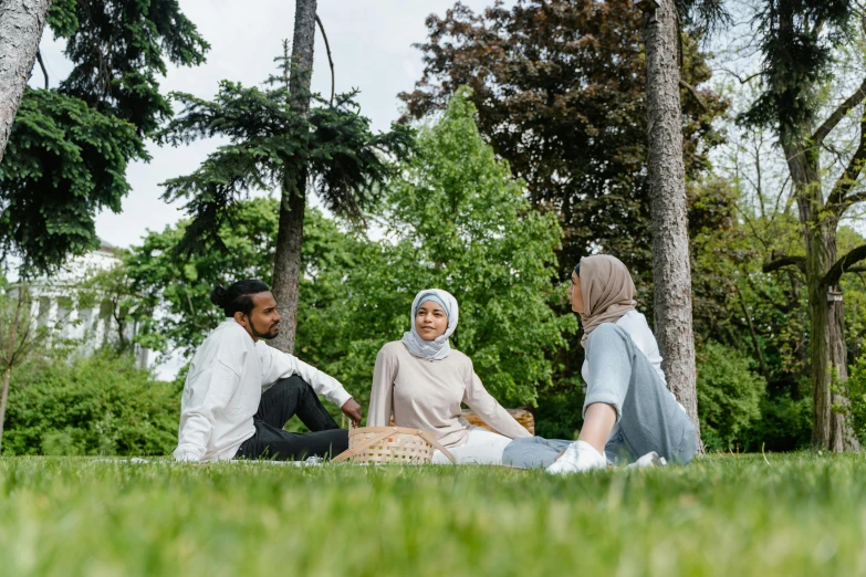 three people sit on the ground near trees and grass
