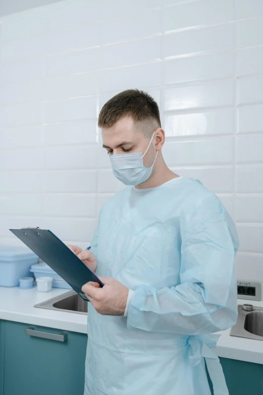 man in blue scrubs holding folder with white face mask